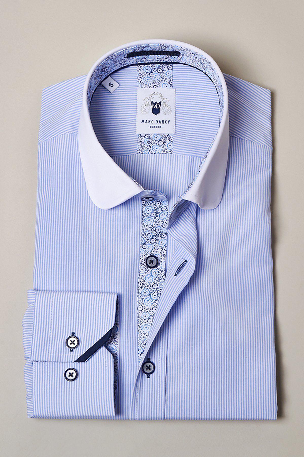 The SHELBY - Sky Blue Stripe Penny Collar Shirt by Marc Darcy features a light blue pin stripe design, white collar, contrasting floral trim on the placket and inner collar, and is crafted from high-cotton fabric. Displayed against a neutral background.