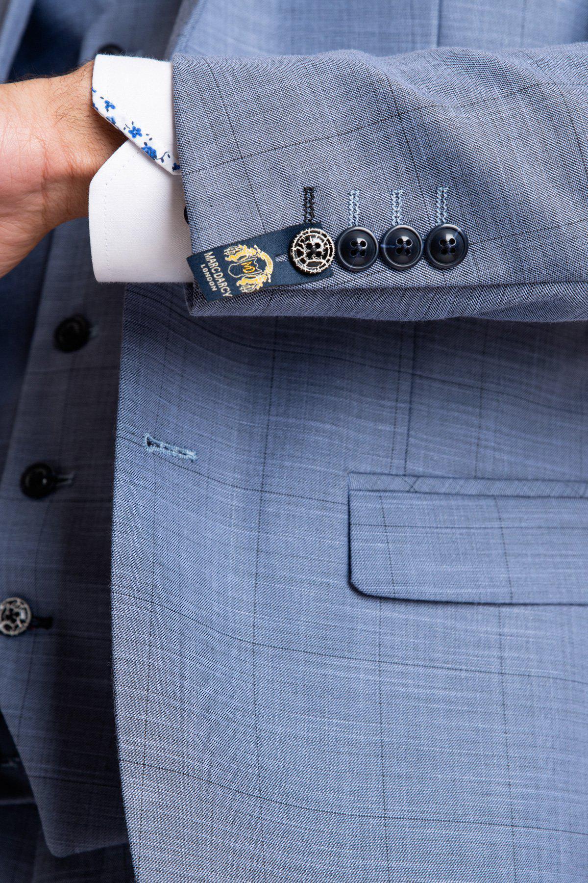 A close-up of a person wearing the marcdarcy SID - Blue Grey Check Blazer, featuring decorative buttons, a dark blue sleeve label, and glimpses of a white dress shirt and pocket.