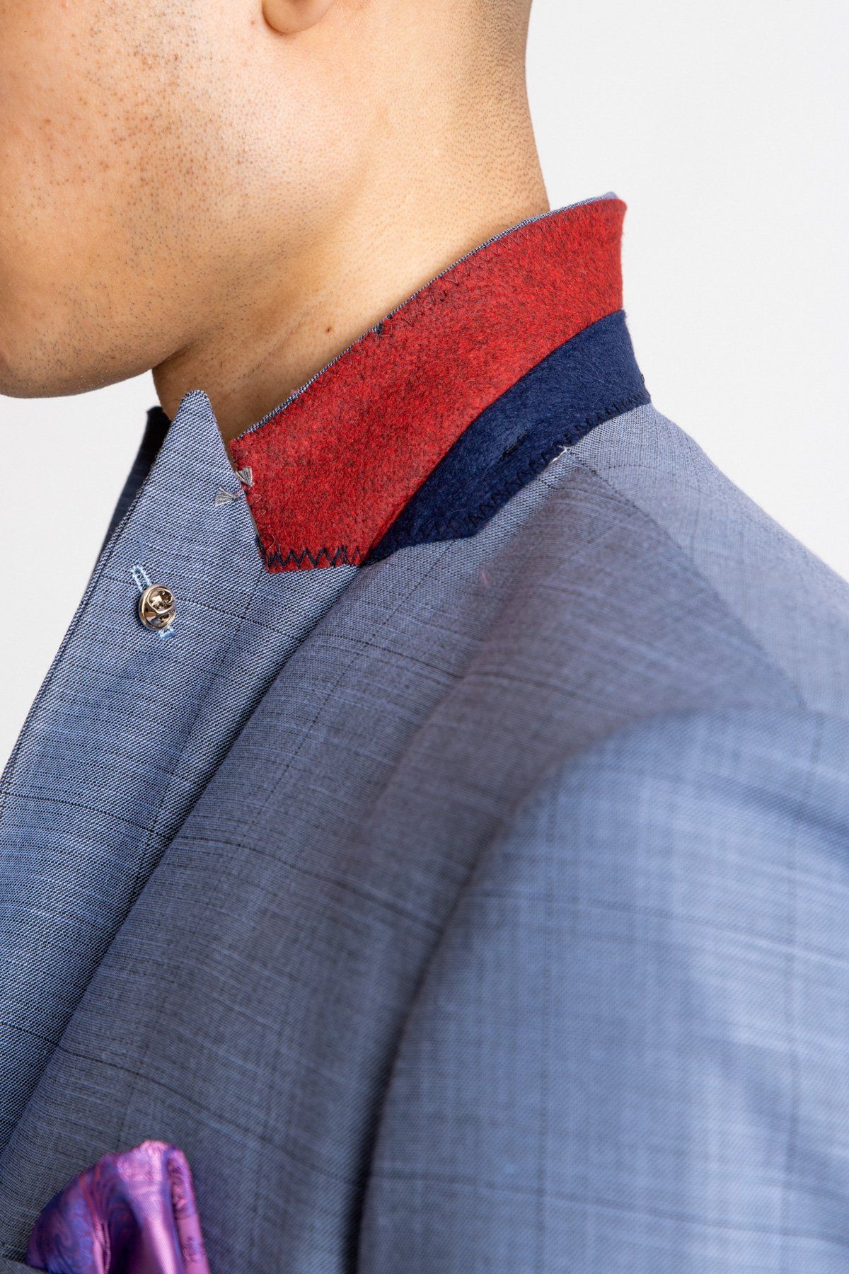 A close-up of a person wearing the marcdarcy SID - Blue Grey Check Blazer, featuring a red and navy contrast collar, silver button, and purple pocket square. Only the side of their face and upper torso is visible.