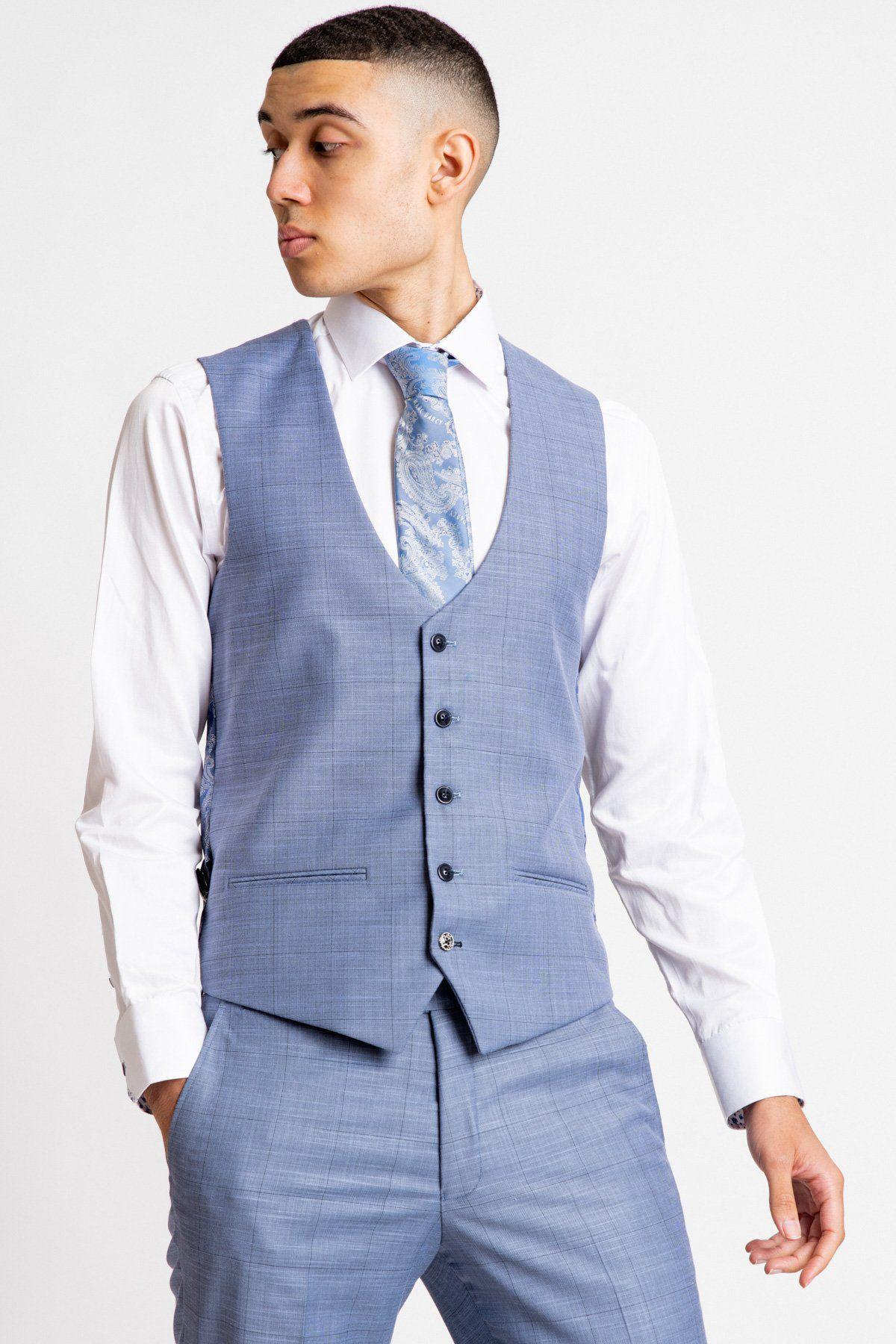 A young man wears the Marc Darcy SID Blue Grey Check Single Breasted Waistcoat with matching trousers, a white shirt, and a patterned tie, standing hands-in-pockets and looking aside against a plain background.