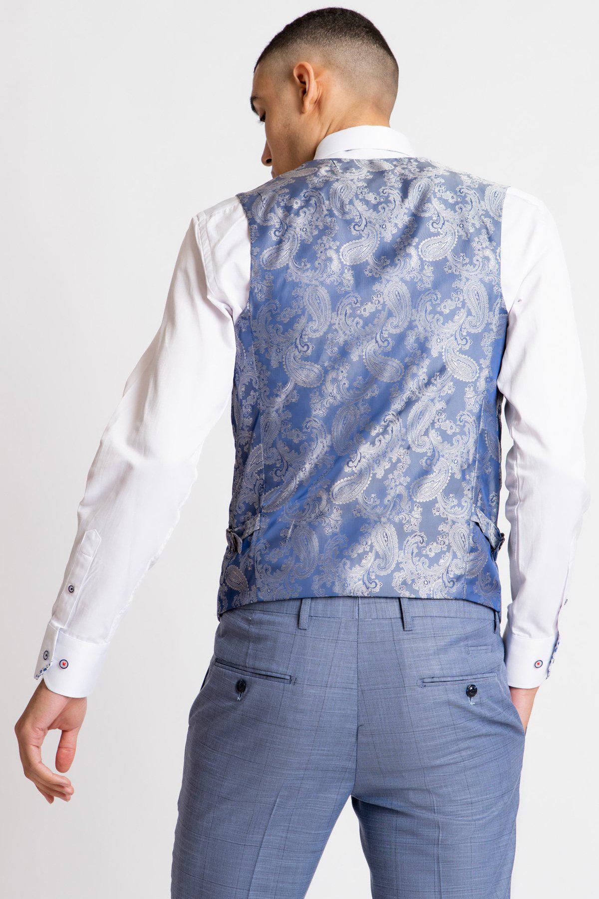 A man stands facing away, wearing a white dress shirt, light blue dress pants, and the Marc Darcy SID - Blue Grey Check Single Breasted Waistcoat. The background is plain and light-colored.