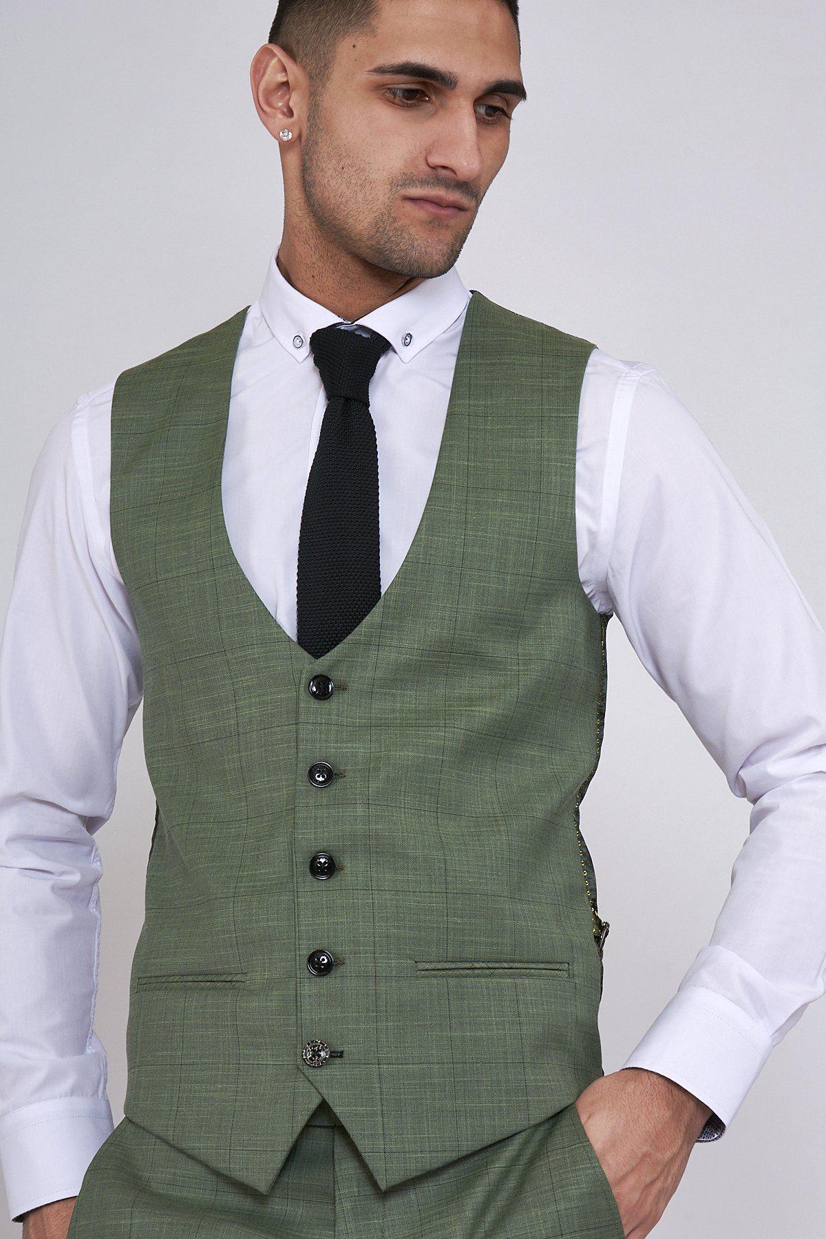 A man models the Marc Darcy SID - Moss Green Check Single Breasted Waistcoat over a white dress shirt and black tie, posing with one hand in his pocket against a plain background.