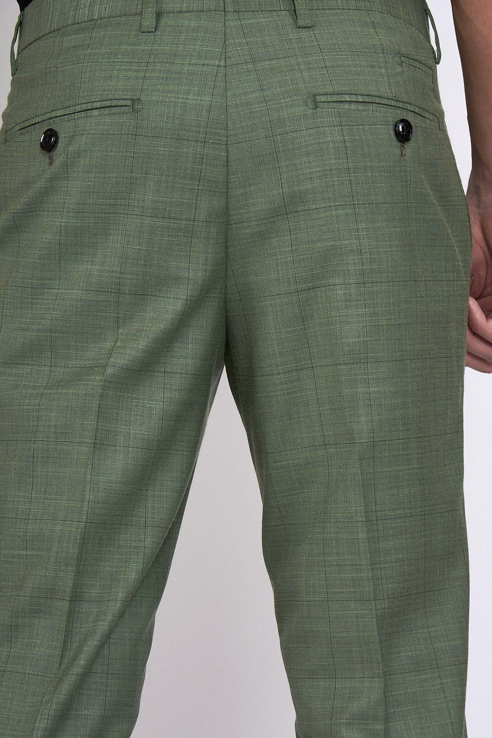 Close-up of the back of a person wearing marcdarcy SID - Moss Green Check Trousers, featuring two back pockets each with a black button; their right hand rests at their side.