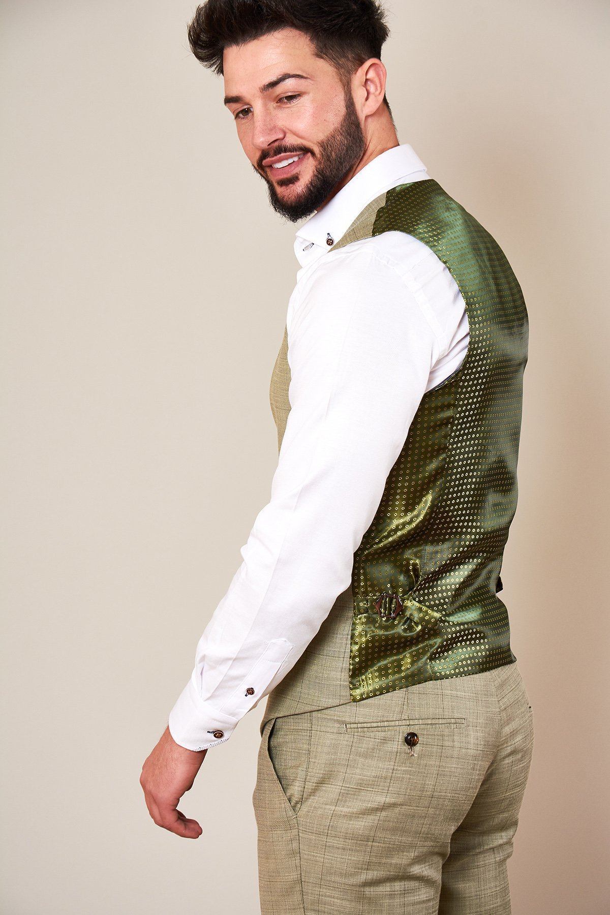 A man with a beard and styled hair wears the Marc Darcy SID - Mustard Beige Check Single Breasted Waistcoat over a white dress shirt, smiling over his shoulder against a plain light background.