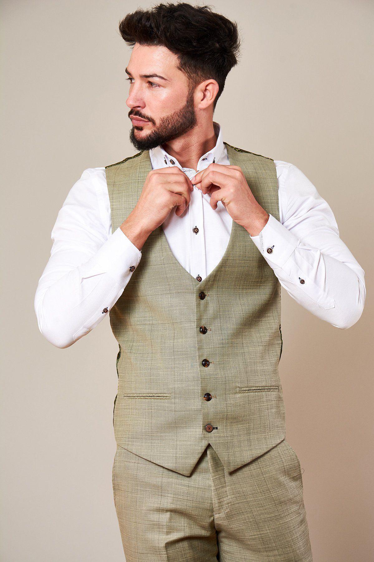 A man with dark hair and a beard adjusts his white shirt collar while wearing the Marc Darcy SID - Mustard Beige Check Single Breasted Waistcoat, paired with matching trousers, looking to the side against a plain background.