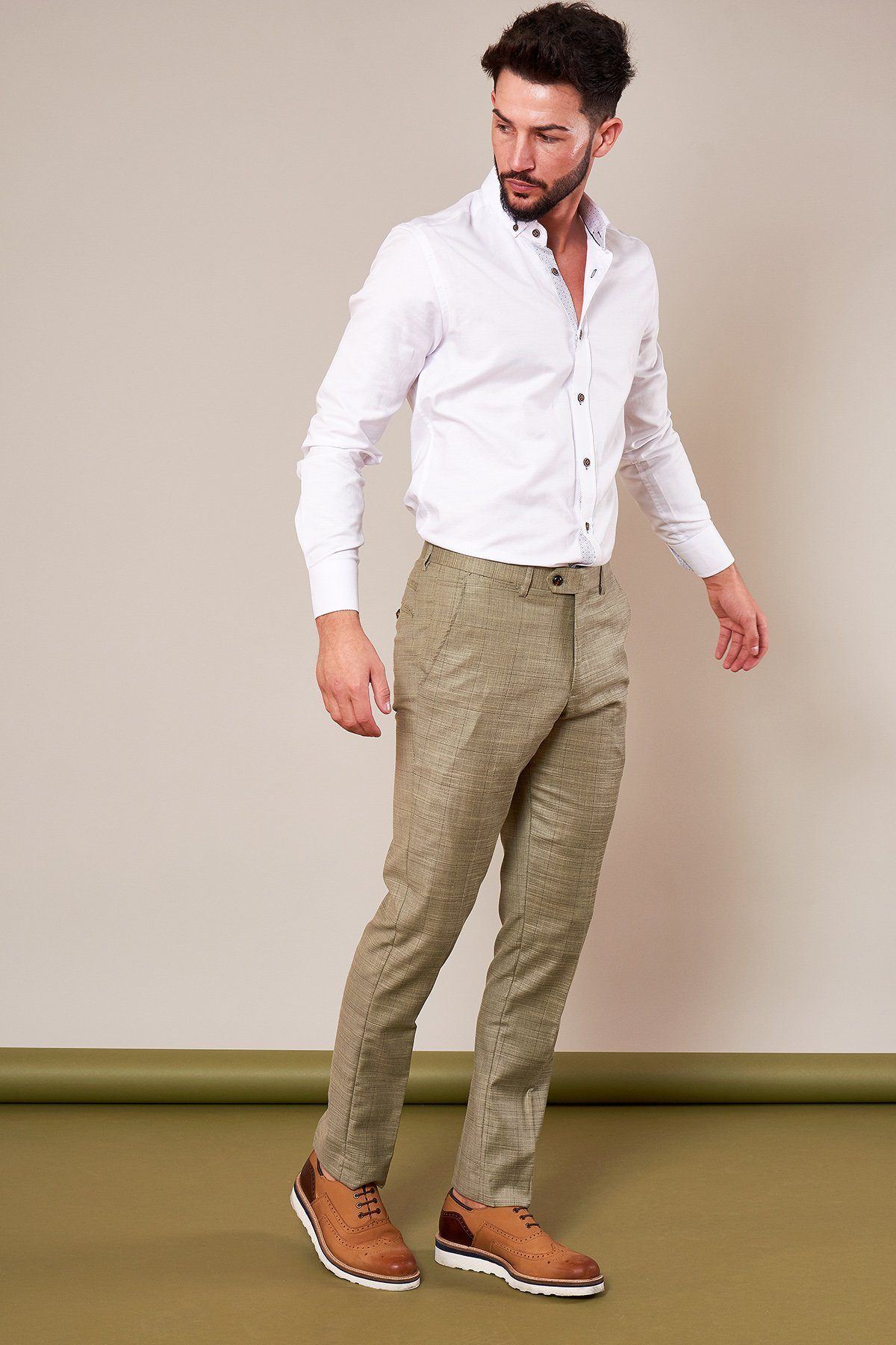 A man with dark hair and a beard wears a white button-down shirt, marcdarcy SID - Mustard Beige Check Trousers, and brown dress shoes, standing against a plain beige background.