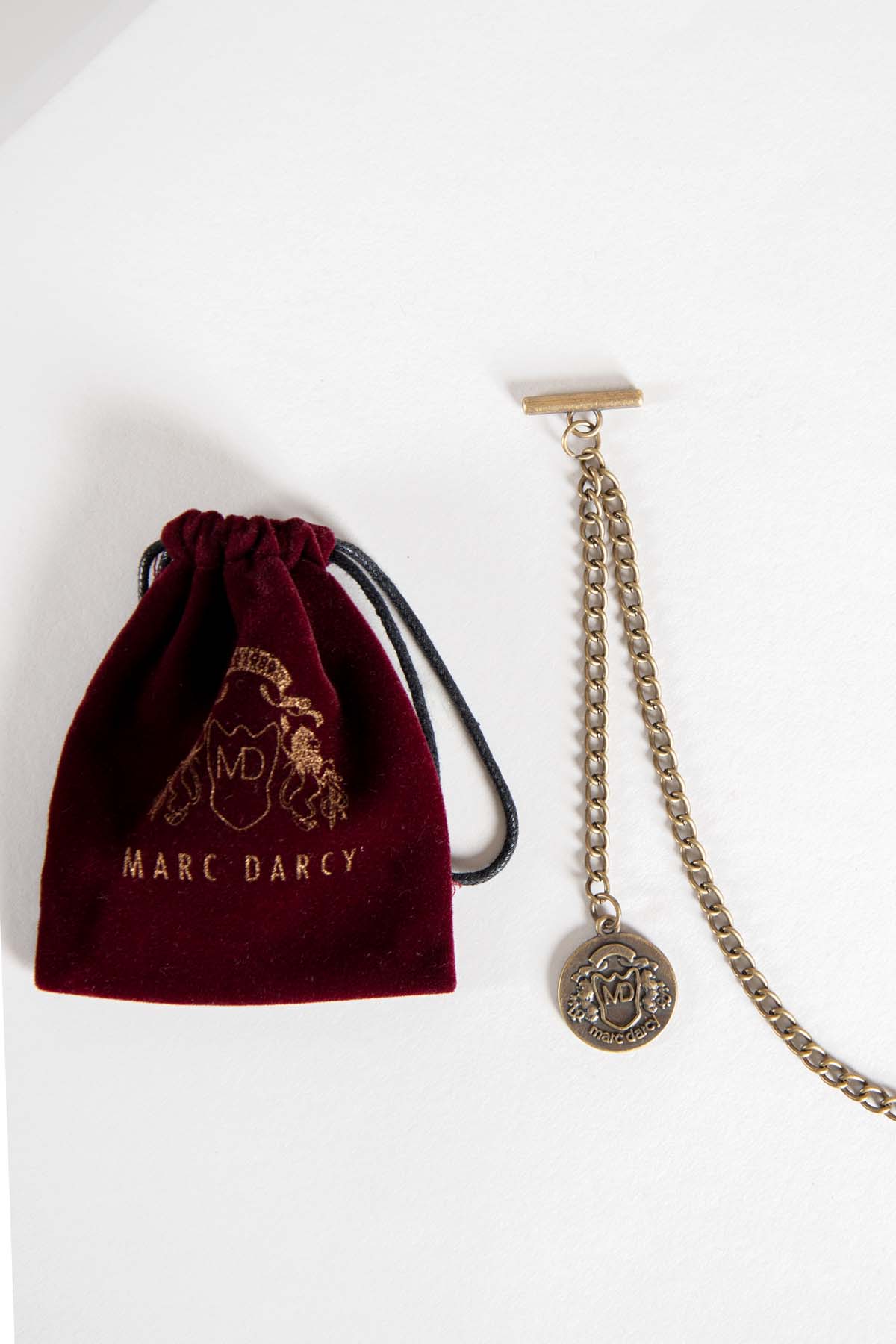 The Antique Style Gold Plated Marc Darcy T-Bar Waistcoat Chain features a dangling coin charm and comes with a maroon MD velvet keepsafe pouch embroidered in gold.