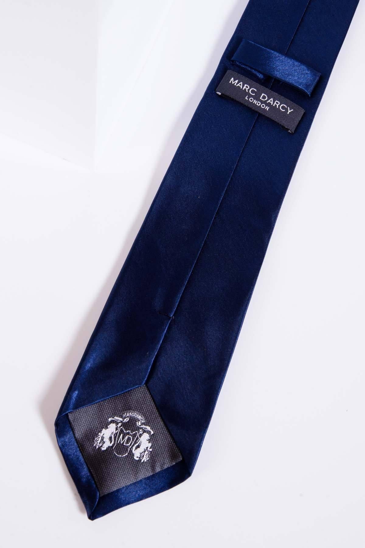 A close-up of the STANLEY - Satin Tie and Pocket Square Set In Navy by Accessory, featuring a navy blue satin tie with a branded label and emblem, laid flat on a white background—perfect for elevating any accessory collection.