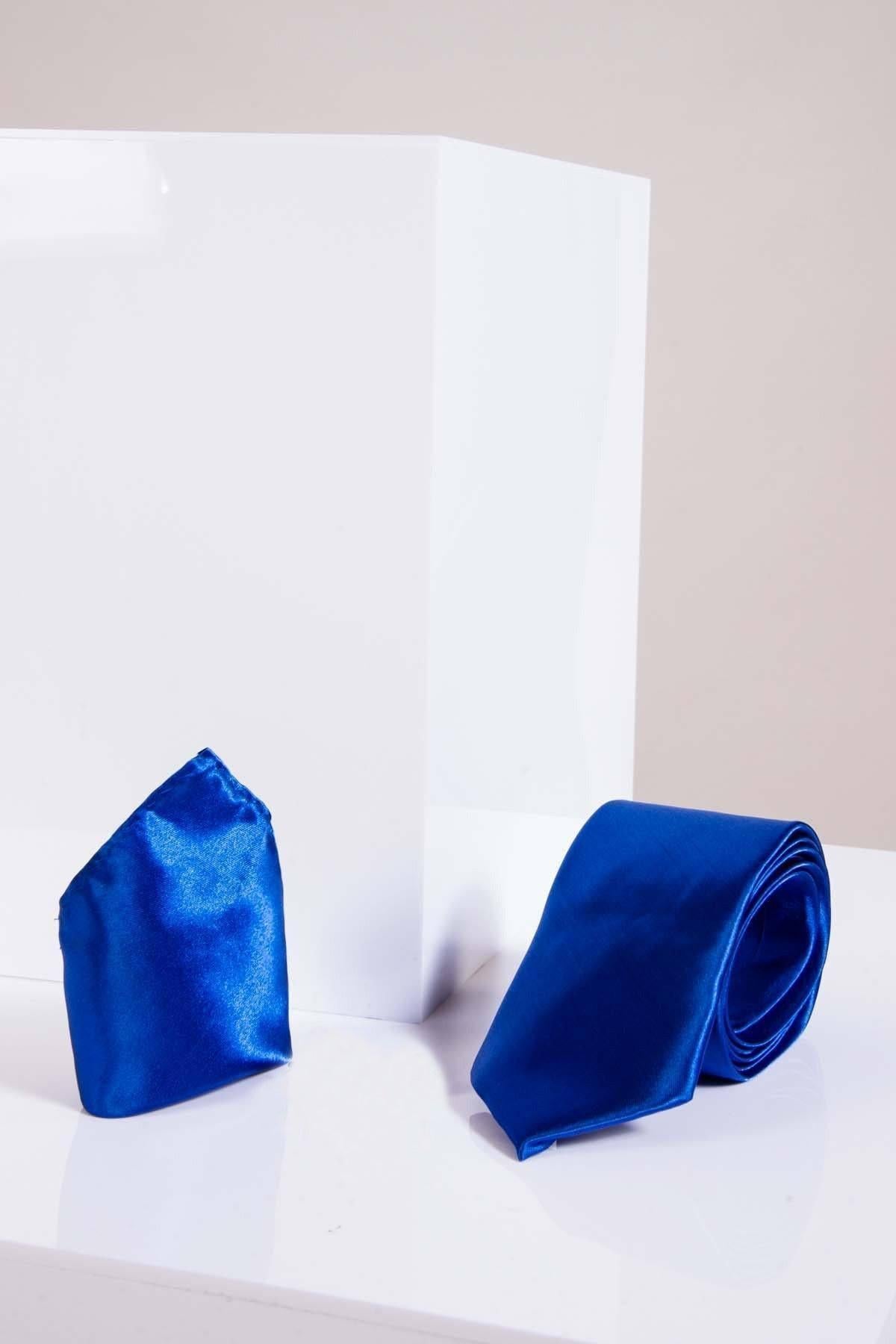 The STANLEY - Satin Tie and Pocket Square Set In Royal Blue by Accessory is shown on a glossy white surface next to a large white rectangular block, all set against a neutral background.