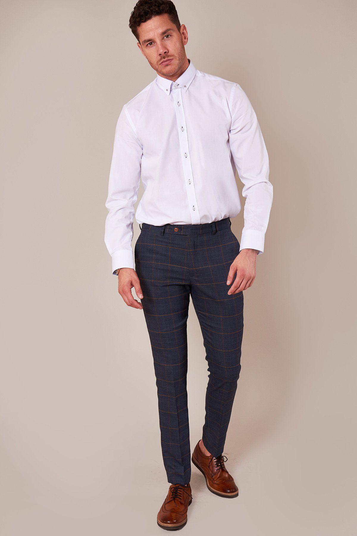 A man with short curly hair and a trimmed beard stands against a plain background wearing the marcdarcy SUTTON white shirt with collar bar, dark blue plaid trousers, and brown dress shoes—an ideal formal look.