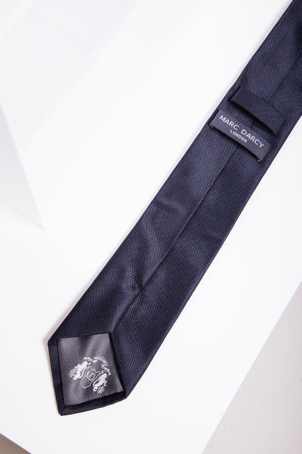 The Marc Darcy TB17 - Birdseye Tie and Pocket Square Set in Midnight features a dark blue textured birdseye print tie with a small white embroidered lion near the tip and a Marc Darcy label on the back.