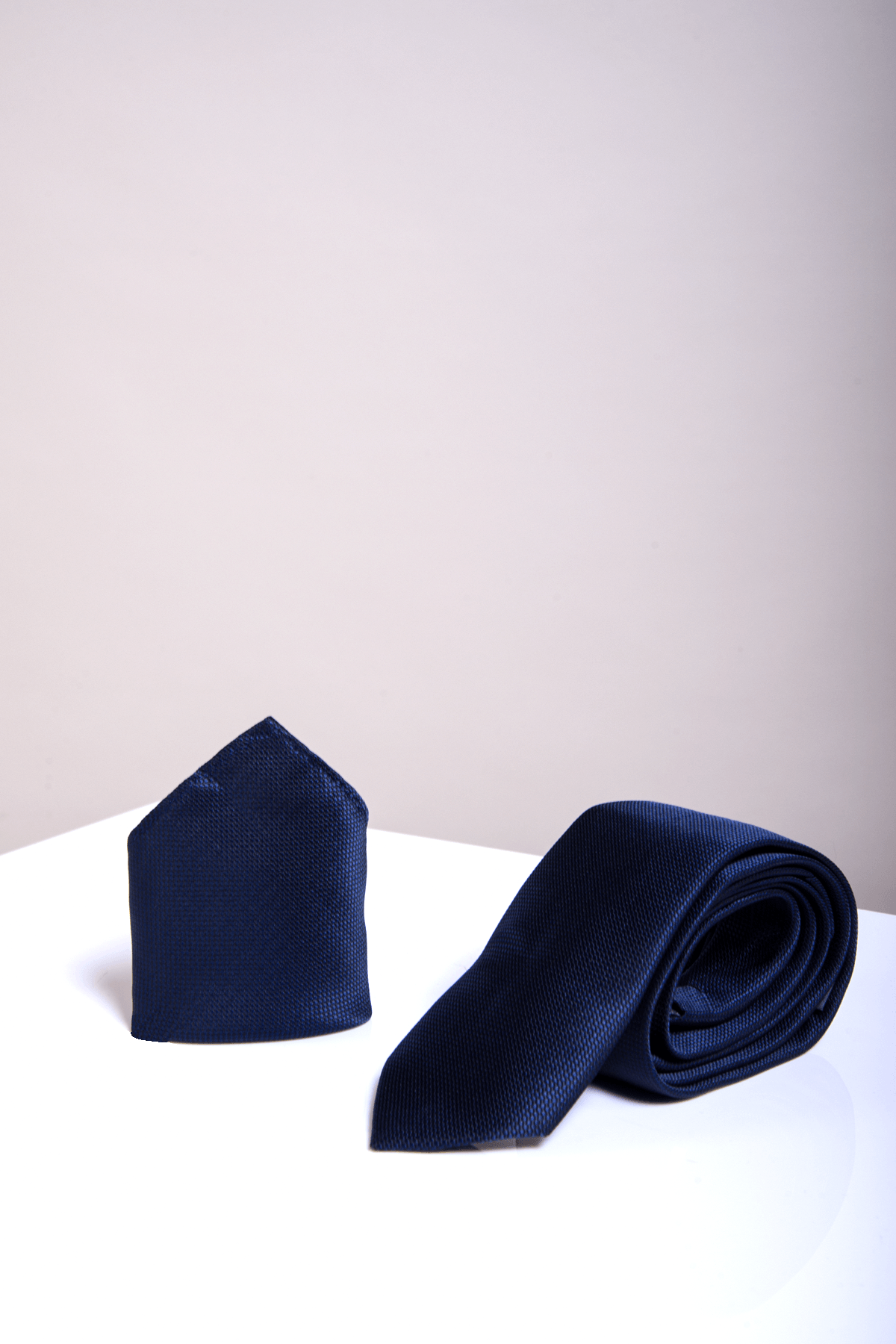 The TOBY Birdseye Tie & Pocket Square Set in Navy by Marc Darcy is displayed upright on a glossy white surface with a pale background.