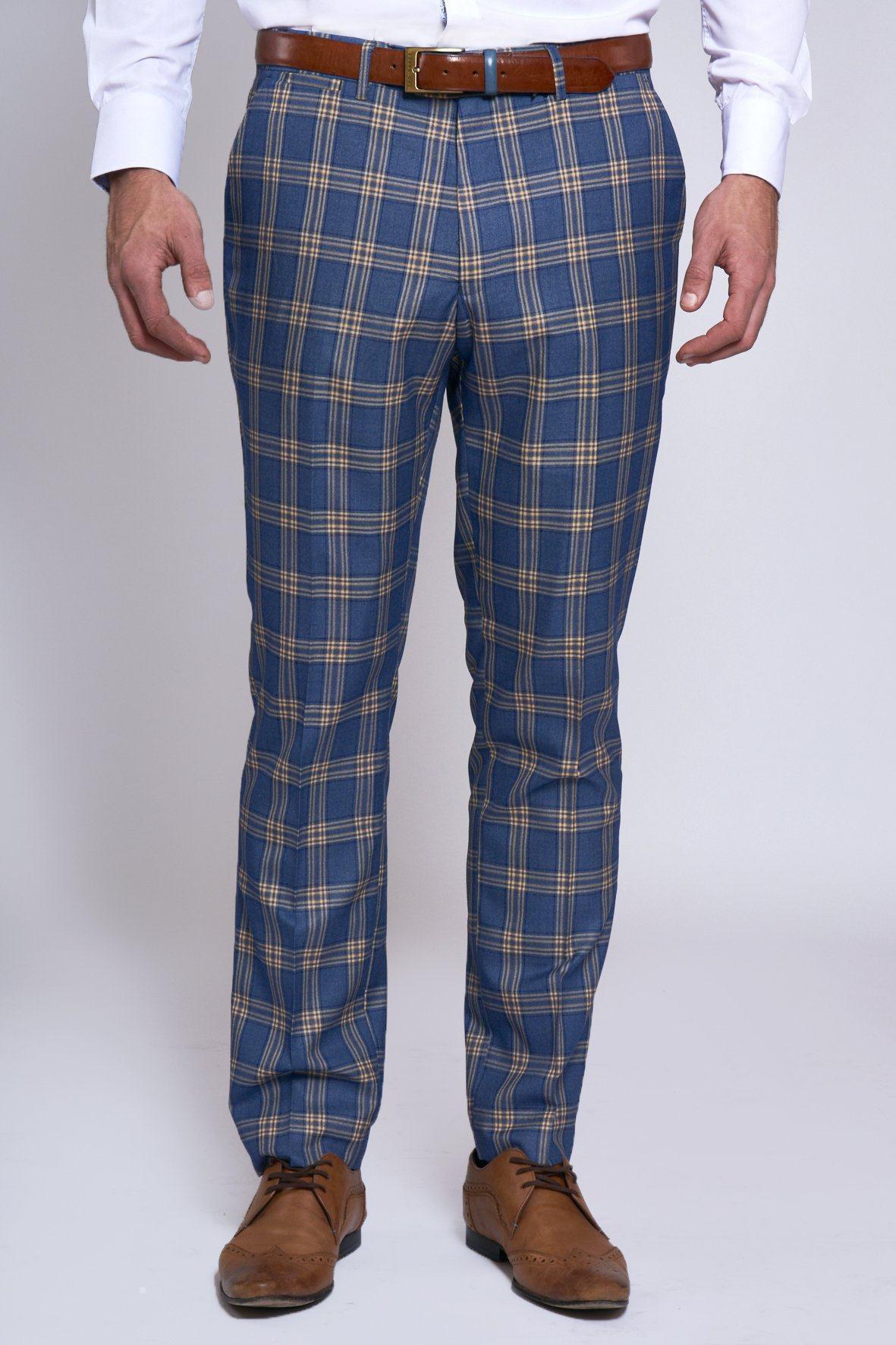 A man wears marcdarcy TONY - Blue Yellow Check Trousers with a brown belt, white shirt, and brown dress shoes, standing against a plain light background.