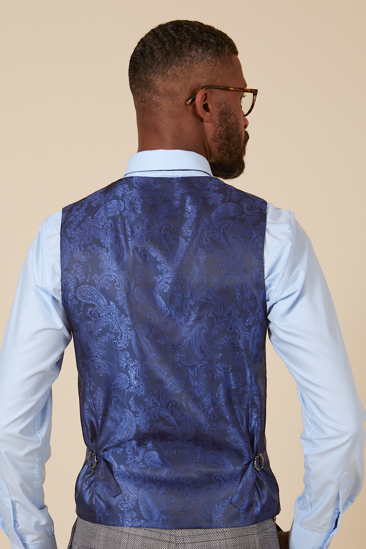 Actor Will Mellor is seen from behind in a marcdarcy Jerry Grey Check Blazer & Waistcoat, wearing glasses and a light blue dress shirt, highlighting the slim fit and adjustable side tabs.