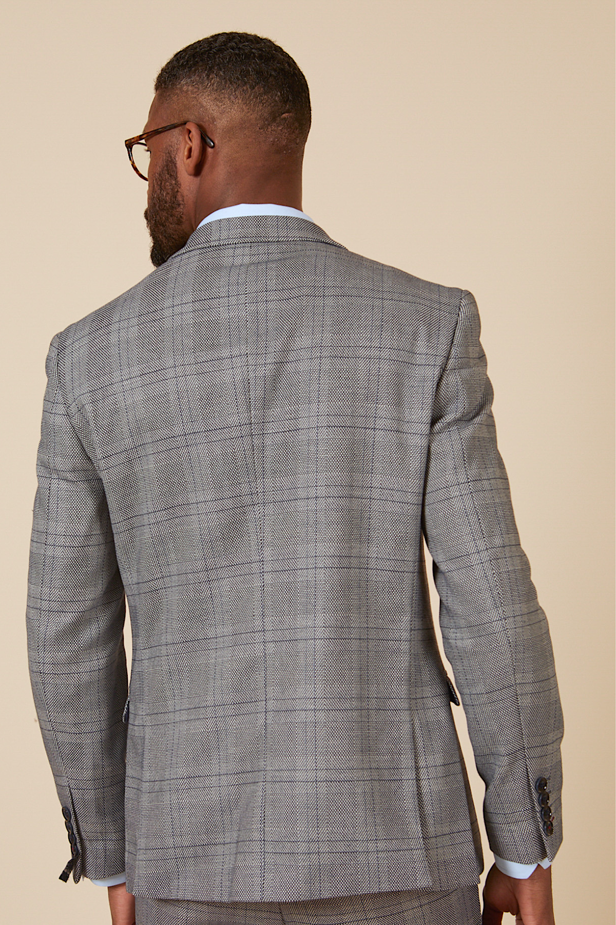 Actor Will Mellor is photographed from behind in a marcdarcy Jerry Grey Check Blazer & Waistcoat, showcasing the back details against a plain beige background.