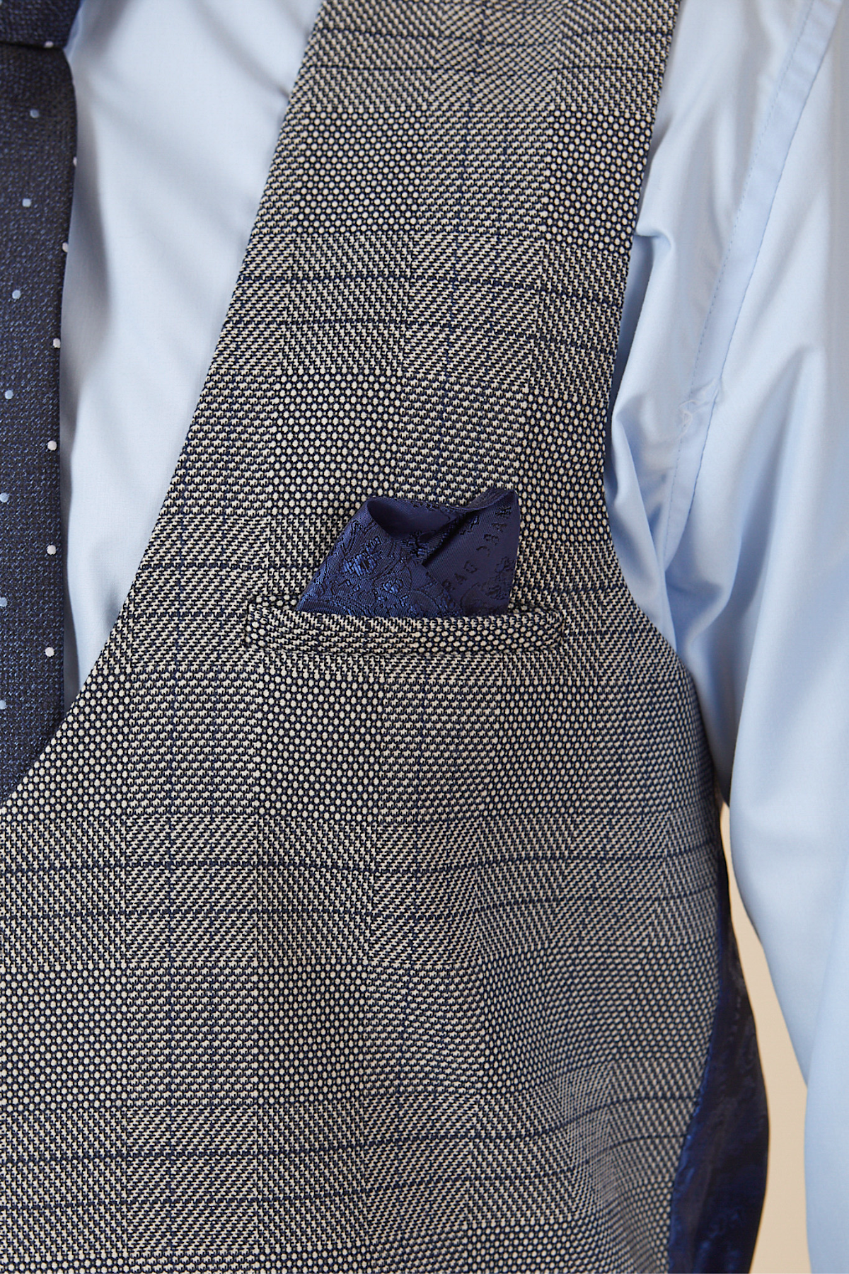 A close-up of actor Will Mellor in a marcdarcy Jerry Grey Check Blazer & Waistcoat, paired with a blue dress shirt, navy dotted tie, and a navy pocket square tucked into the vest pocket.