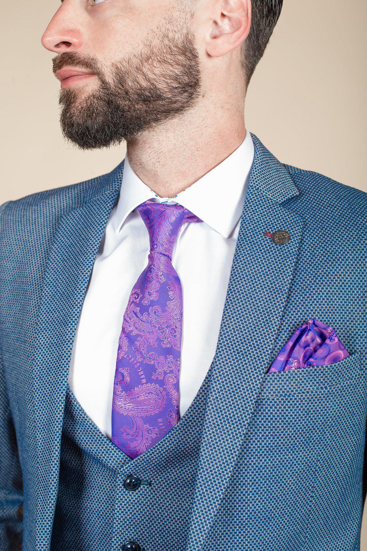 A man in a marcdarcy WILSON - Blue Birdseye Blazer, paired with a white dress shirt and a purple paisley tie with matching pocket square, looks to the side.