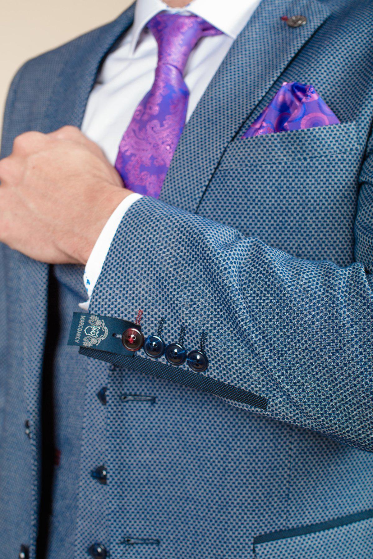 A man in the marcdarcy WILSON - Blue Birdseye Blazer with matching vest, white shirt, purple paisley tie, and a purple pocket square adjusts his jacket.