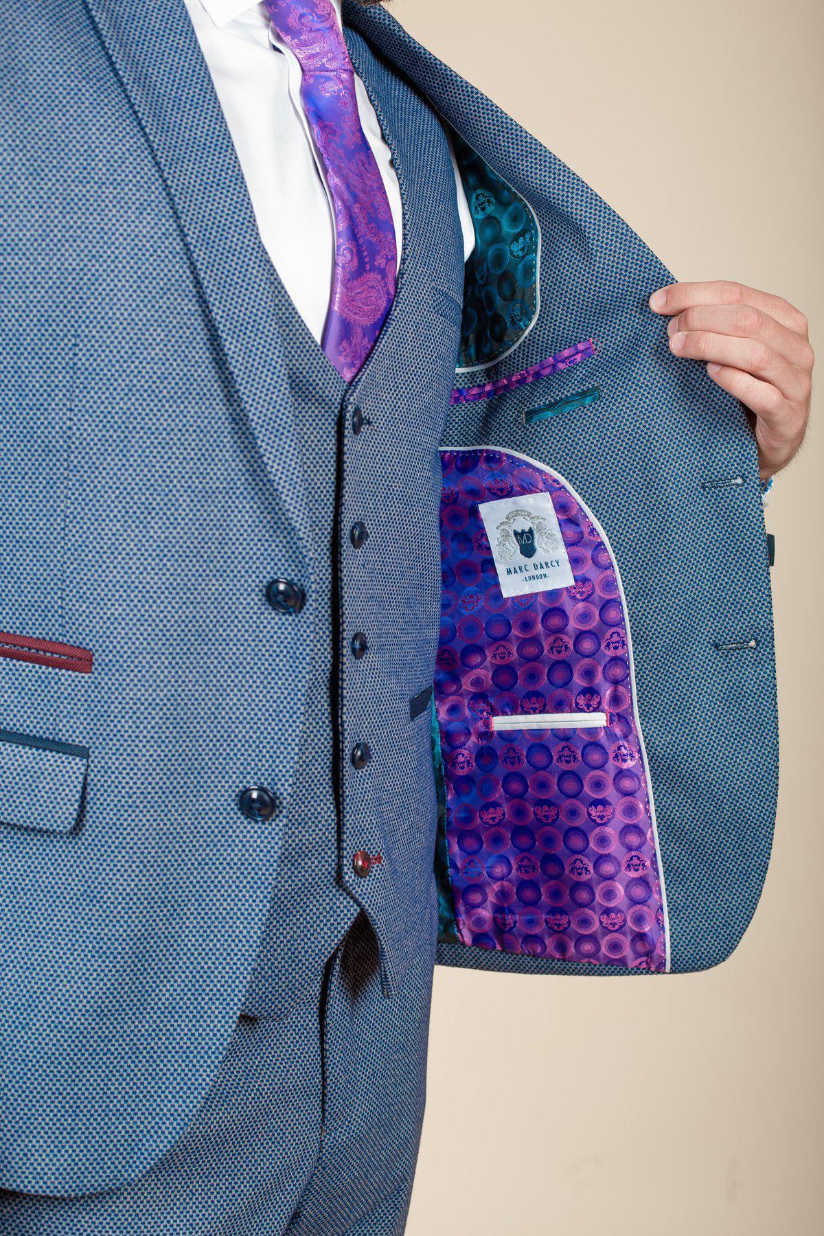 Wearing the marcdarcy WILSON - Blue Birdseye Blazer and a purple patterned tie, a person holds open their slim fit jacket to show off its vibrant purple and blue lining and a visible inside clothing label.