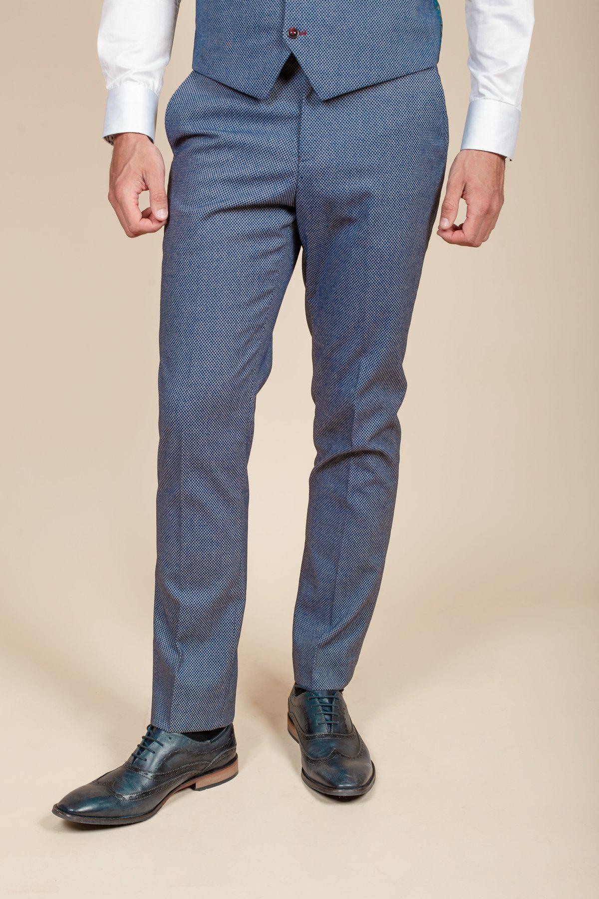 A man wears marcdarcys WILSON - Blue Birdseye Trousers with a matching vest, white shirt, and black leather dress shoes against a beige background. His face is not visible.